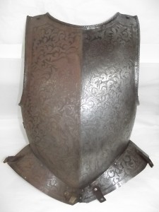Breast plate from a suit of armour possibly dating back to the 15th century.  The breast plate is decorated with a floral pattern like the “mantling”, or drapery, of a coat of arms.  The decorative design is completed by a knight in a full suit of armour and a mythical phoenix. The breast plate was covered in a heavy layer of red iron corrosion which was disfiguring the surface of the armour and if left could have led to extensive damage. For the purpose of this display the corrosion has been removed from one half of the breast plate, and it has been left in place on the other half in order to highlight the difference.  The corrosion will be completely removed from the breast plate when the armour is removed from this display. 