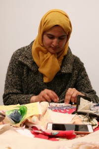 Woman in headscarf and coat working at table full of fabric pieces
