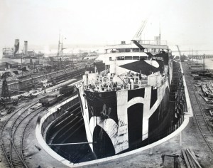 Photograph of dazzle painted oil tanker Cadillac undergoing repairs at Smith’s Dock yard at North Shields on the River Tyne. Cadillac was built by Palmer’s Ship Building & Iron Co. Ltd., Hebburn-on-Tyne and completed in December 1917. On 7th April 1918 she was torpedoed and damaged by U-53 about 100 miles WSW of Bishop Rock. Cadillac was one of Wilkinson’s dazzle ships that made port after a U boat attack. I think it is a fair bet that the repairs are for the damage caused by U-53’s torpedo. (TWCMS : 1993.9590 – Smith’s Dock Notable War Jobs album) 