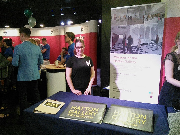 Woman standing at indoor stall promoting Hatton Gallery