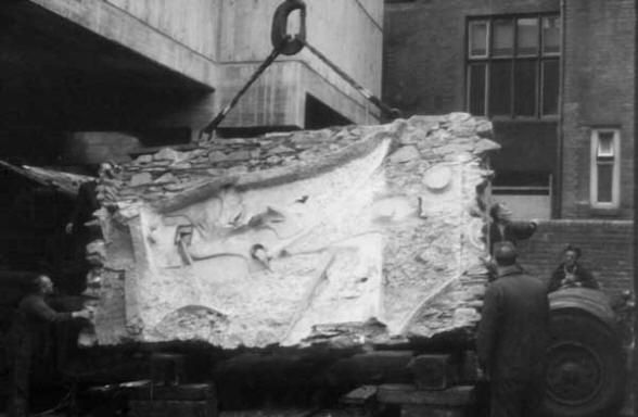 Old black-and-white photo of large abstract square wall sculpture being lifted off a the back of an open truck by a lifting hook and strap