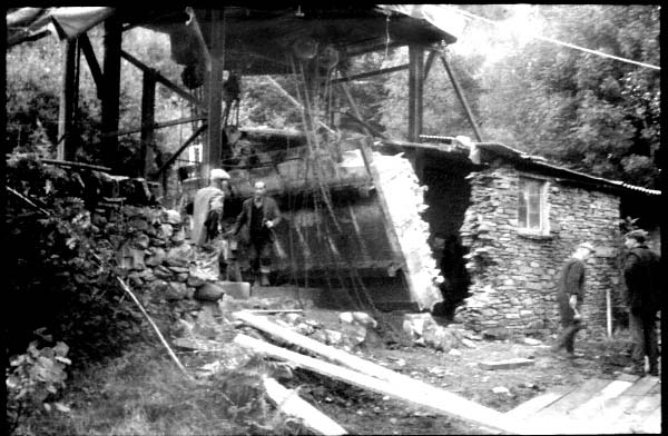 Vintage black and white exterior photo of group of men removing a large section of wall from a smallstone outbuilding